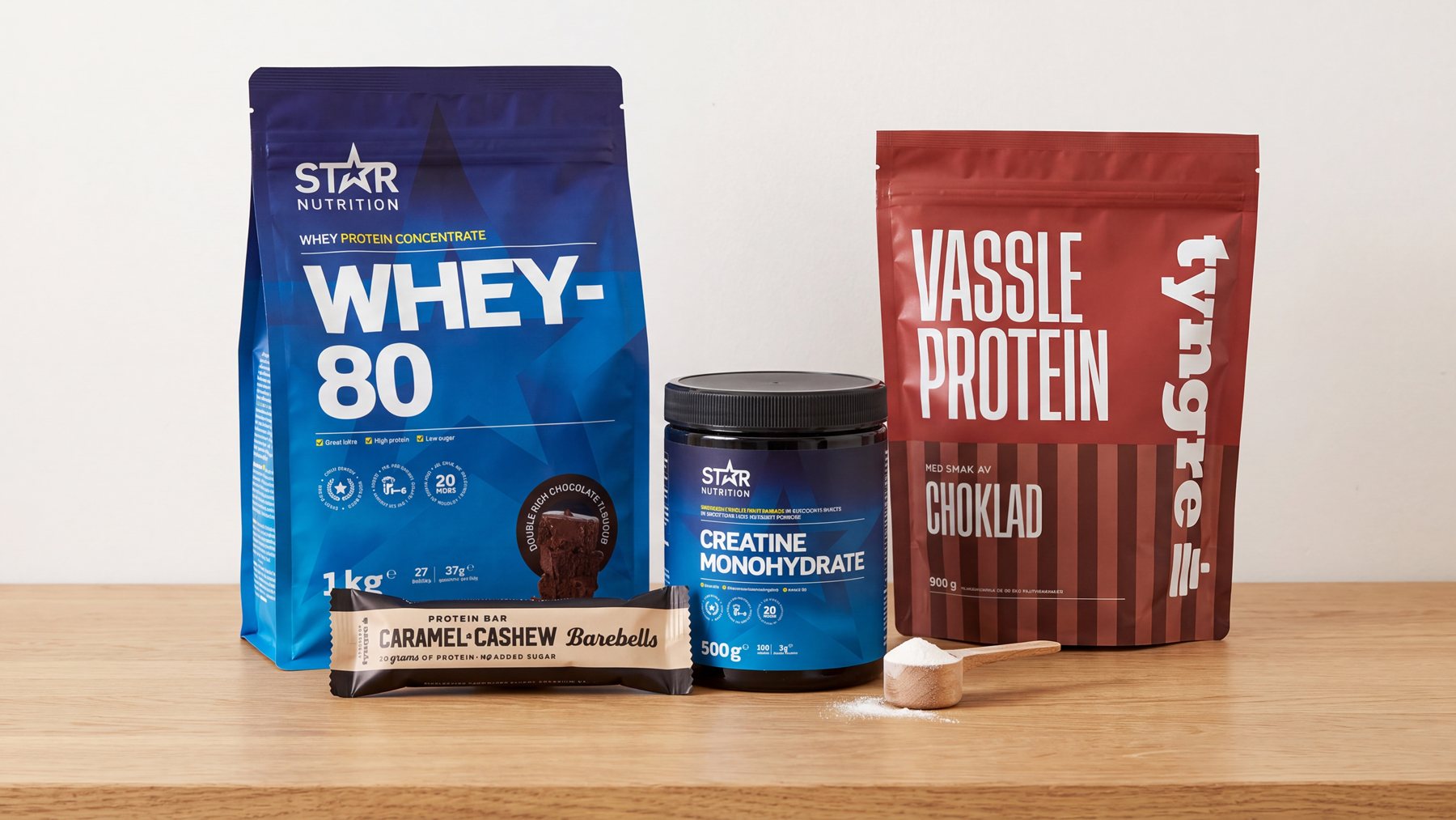 Star Nutrition Whey-80, Star Nutrition Creatine Monohydrate, Tyngre vassleprotein choklad och en Barebells proteinbar på en köksbänk